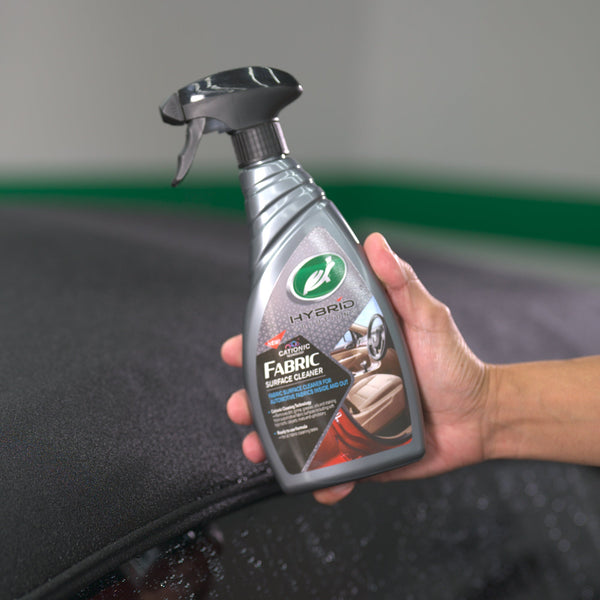 Hand holding Turtle Wax Hybrid Solutions Fabric Surface Cleaner for auto interiors/exteriors.