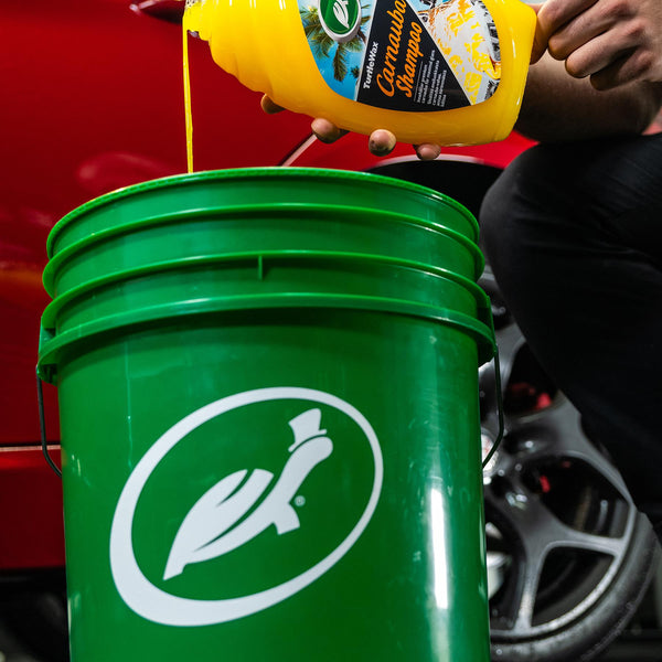 Turtle Wax carnauba shampoo pouring into a green bucket with the brand's running turtle logo for auto detailing.