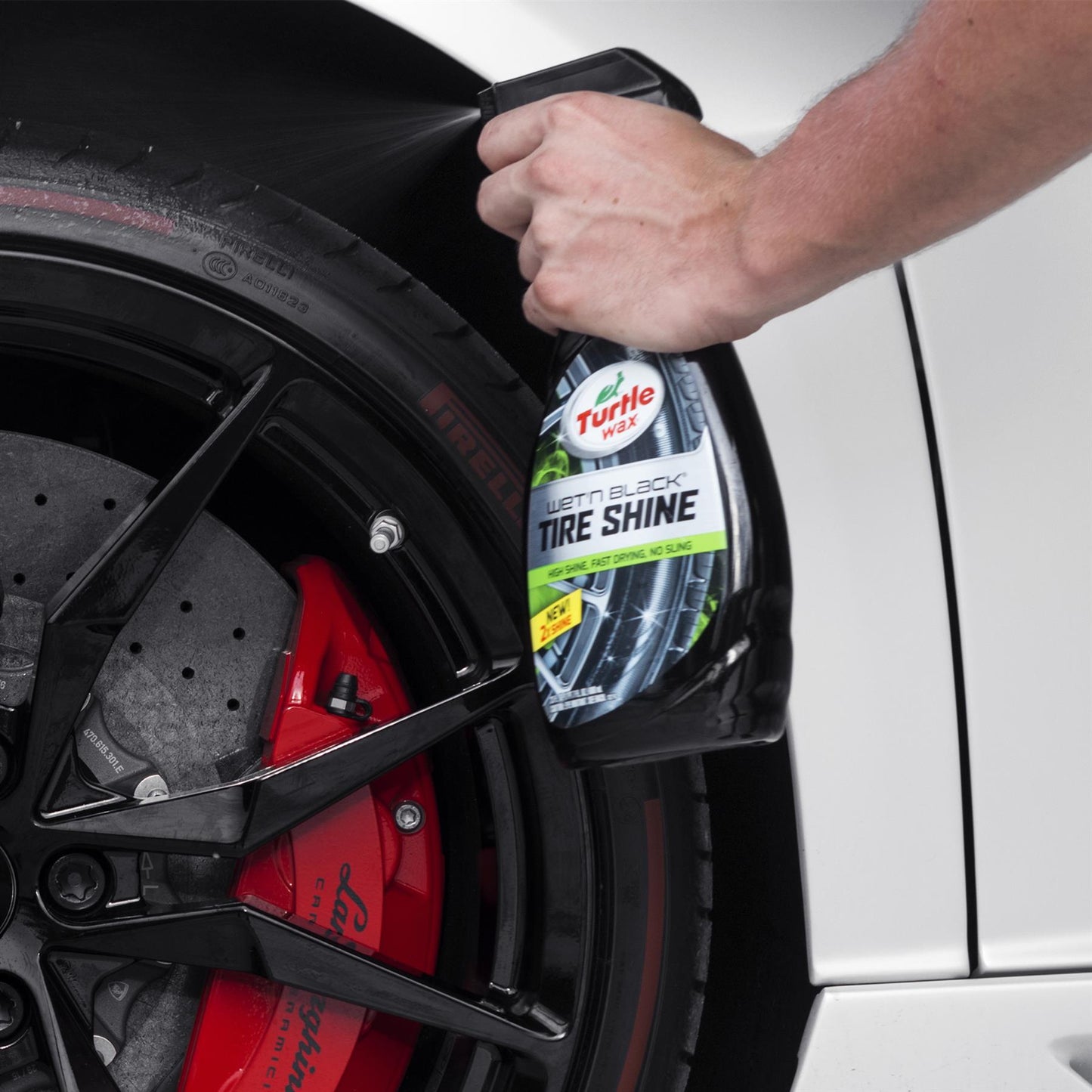 Turtle Wax tire shine being sprayed on a car tire with red Lamborghini branded brake calipers.