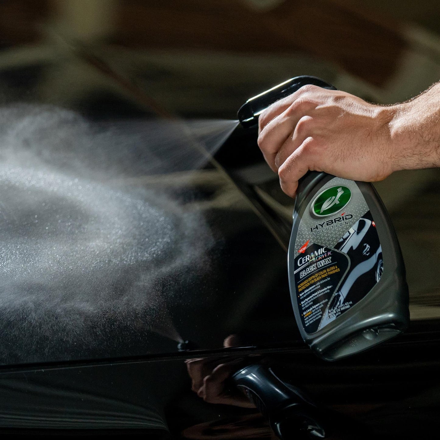 Turtle Wax Hybrid Solutions Ceramic Acrylic Black Wax being sprayed on a black vehicle. Car care product application.