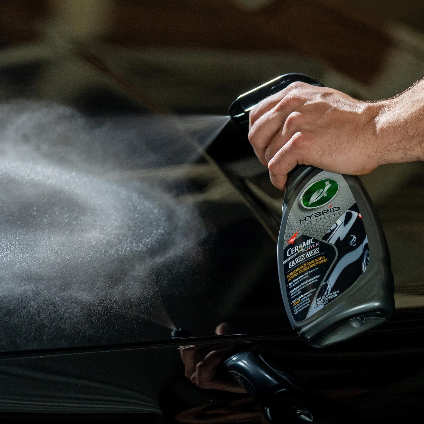 Turtle Wax Hybrid Solutions Ceramic Acrylic Black Wax being sprayed on a black vehicle. Car care product application.