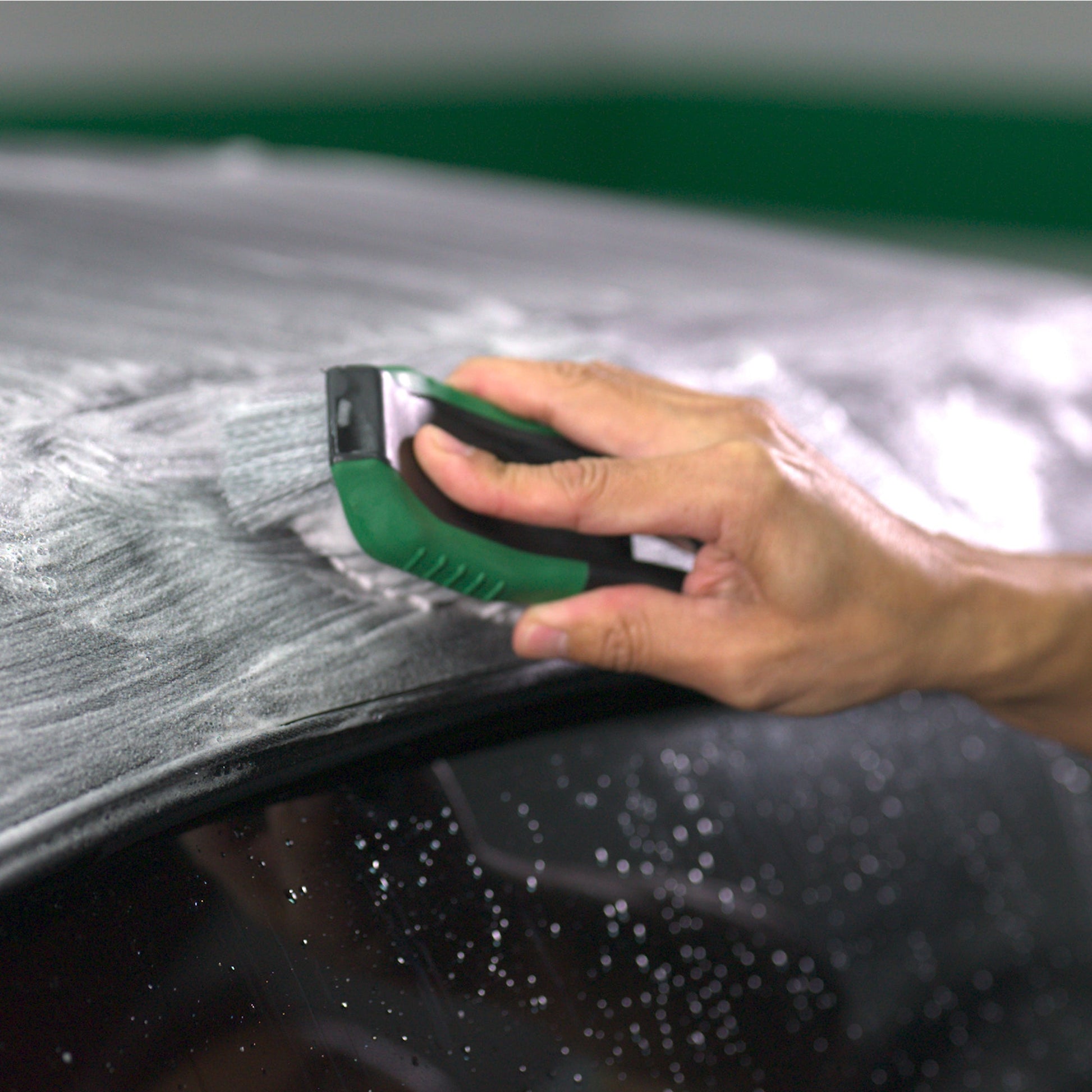 Cleaning car interior. Hand uses a green-handled brush on foamy, cleaned fabric.