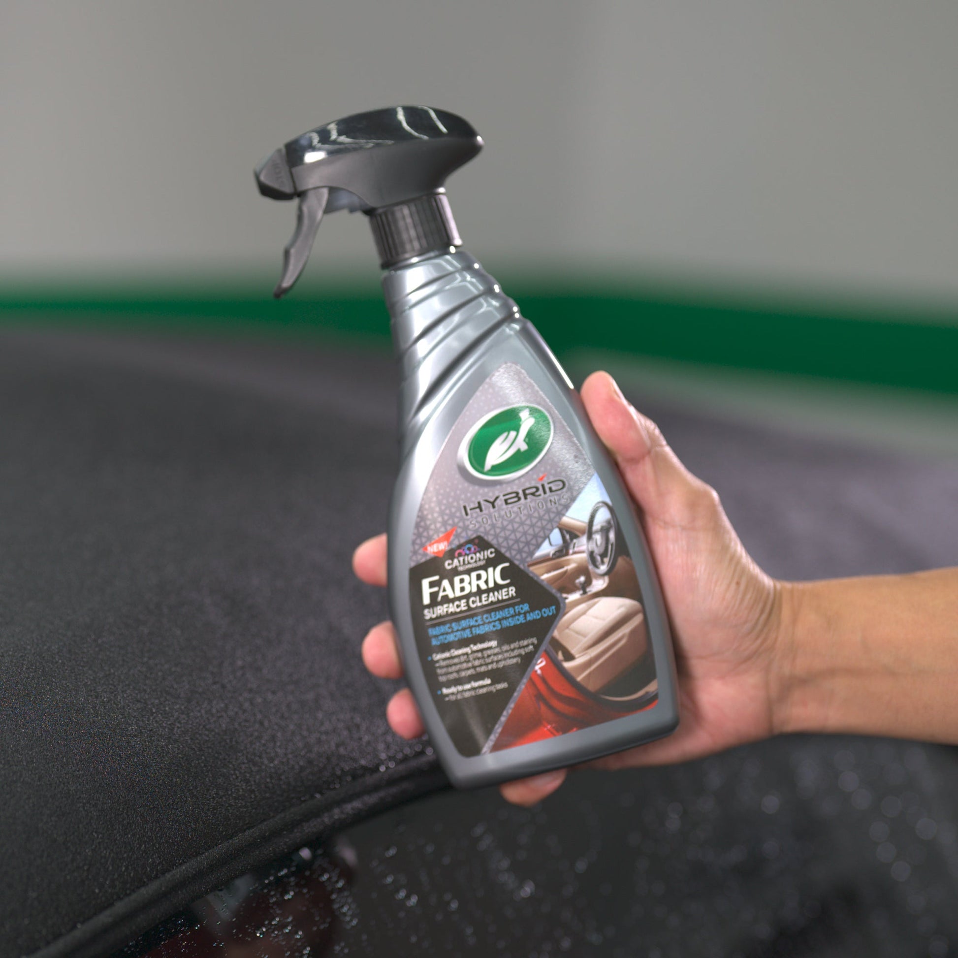 Hand holding Turtle Wax Hybrid Solutions Fabric Surface Cleaner for auto interiors/exteriors.