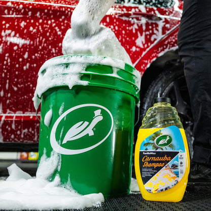 Red car being washed with foamy Turtle Wax Carnauba Shampoo, shown next to a green Turtle Wax bucket.