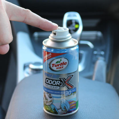 Finger pushing aerosol car air freshener, Turtle Wax brand, on vehicle console. Caribbean scent, for odor elimination in Indian cars.