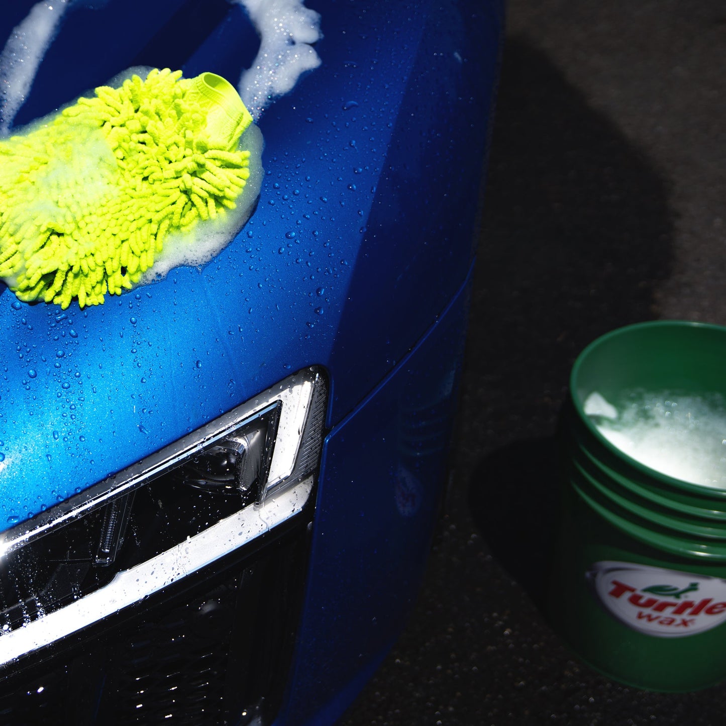 Blue car cleaning in progress! See the foam and water droplets with washing mitt and a Turtle Wax bucket nearby.