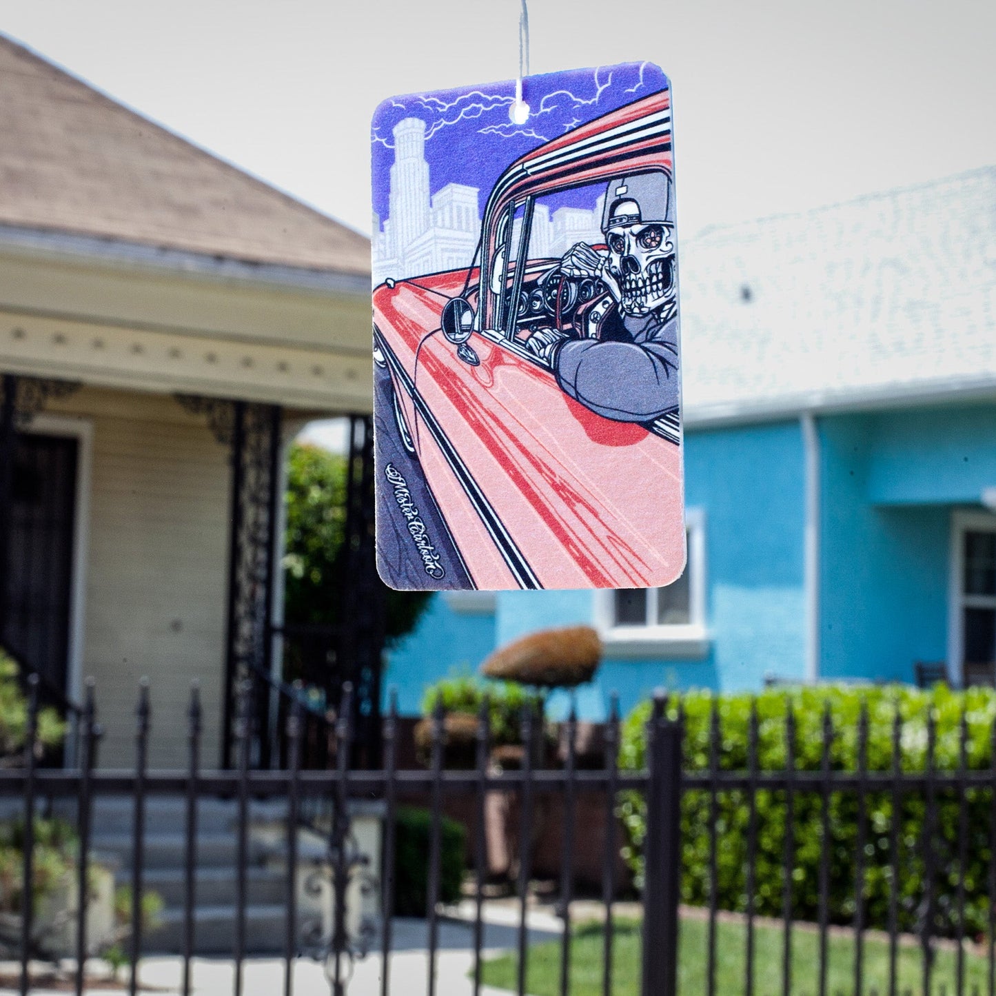 Hanging car freshener. Skeleton driver, red car, city backdrop, and lightning.