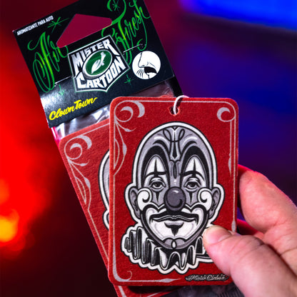 लाल रंग के कार पेपर फ्रेशनर पर जोकर का चेहरा है, "क्लोन टाउन" के सुगंधित डिब्बे के साथ।