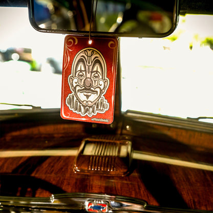 कार के अंदर पेपर एयर फ्रेशनर। लाल रंग का जोकर डिजाइन वाला, डैशबोर्ड पर लटका हुआ।