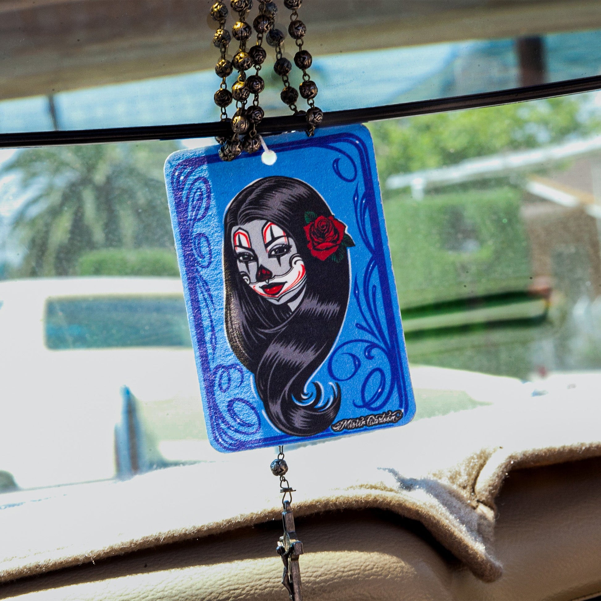 Car air freshener with a La Catrina design hangs from the rearview mirror with a rosary.