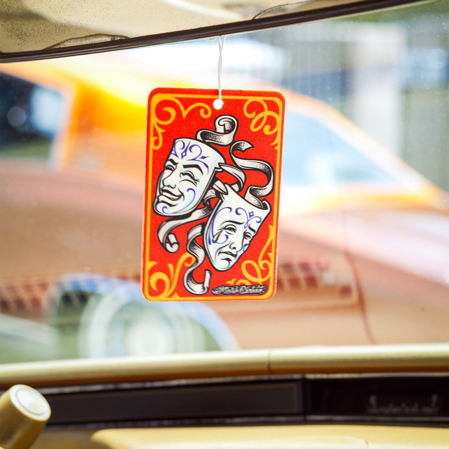 Car interior view: Natak masks (Comedy & Tragedy) themed fragrance hanging. Vehicle background is visible through the window. #fragrance #car #indian