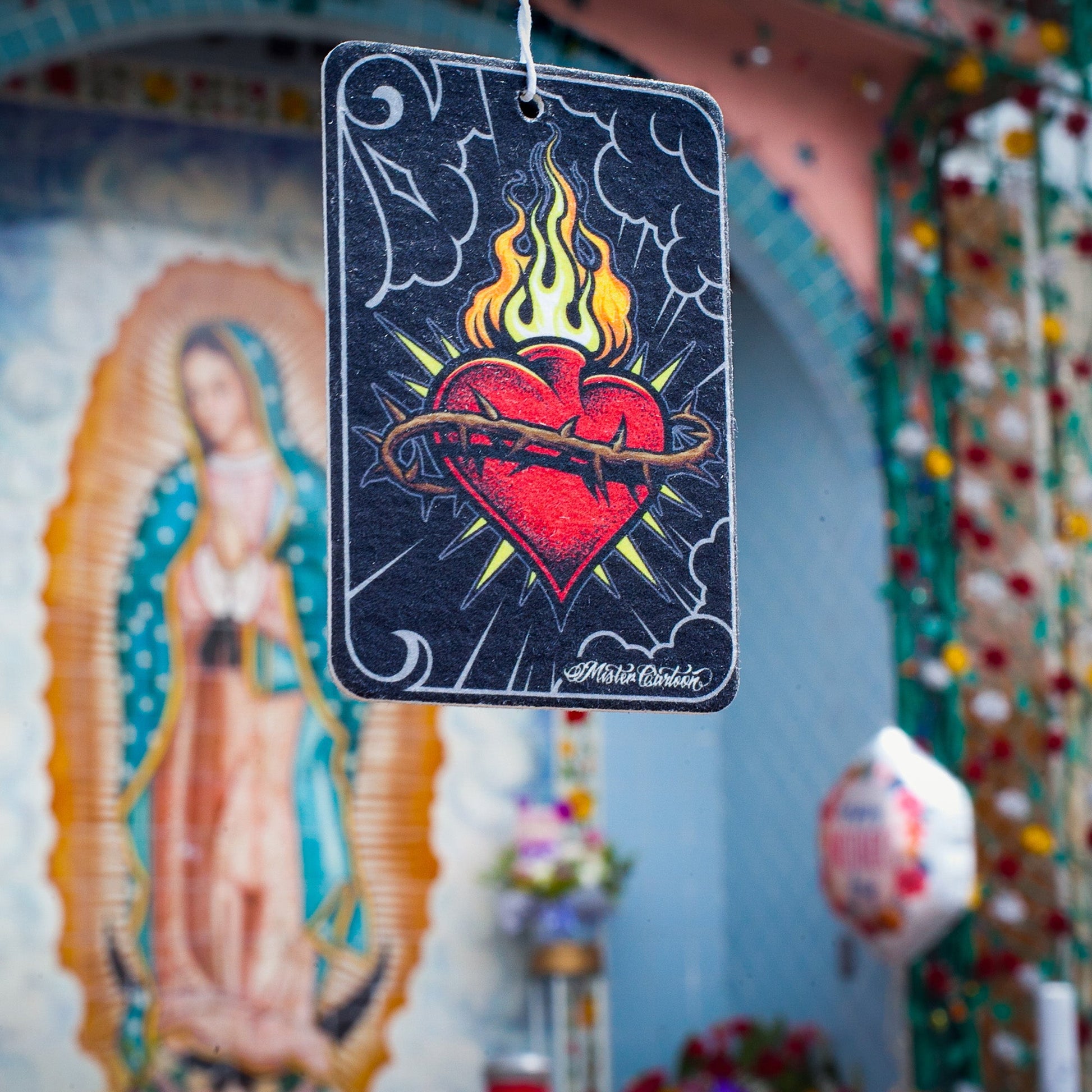 Paper air freshener featuring a flaming sacred heart with thorns, against an Our Lady of Guadalupe devotional background.