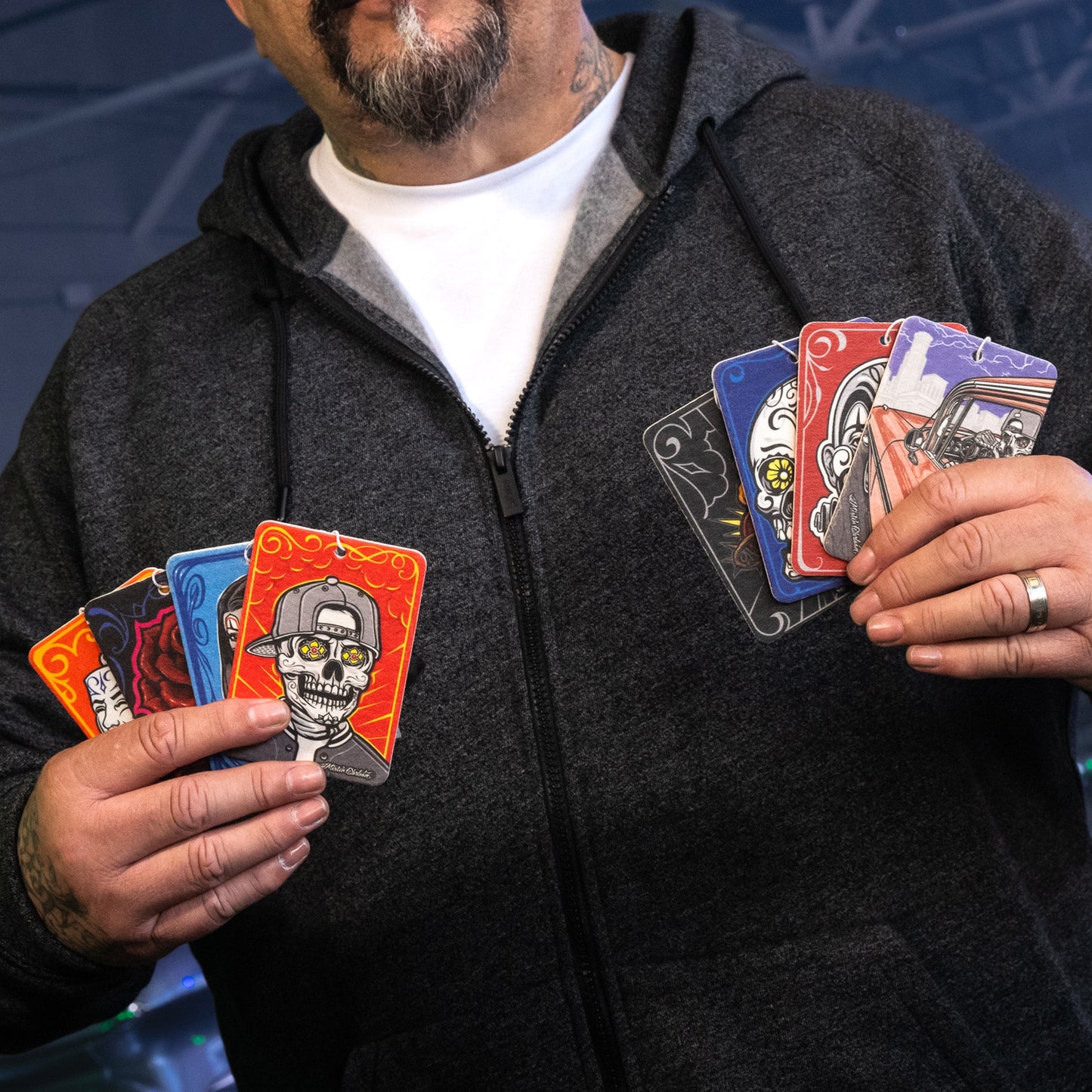 Man holds Sacred Soul paper air fresheners. Automotive accessories with skull & car designs. Home and car freshness.