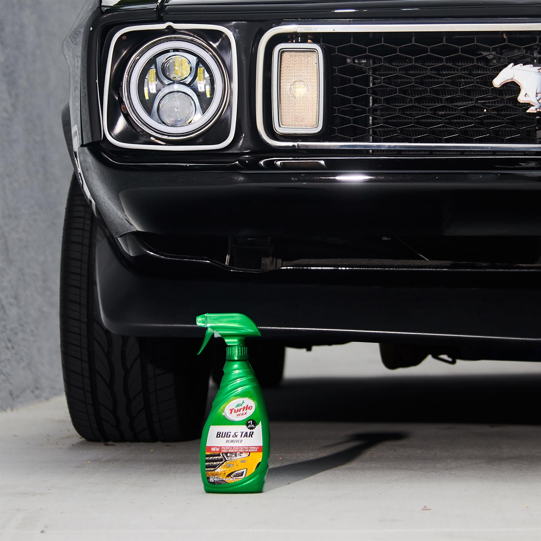 Turtle Wax Bug & Tar Remover near classic black car's headlight and grill. Mustang pony logo visible. Car care in India.