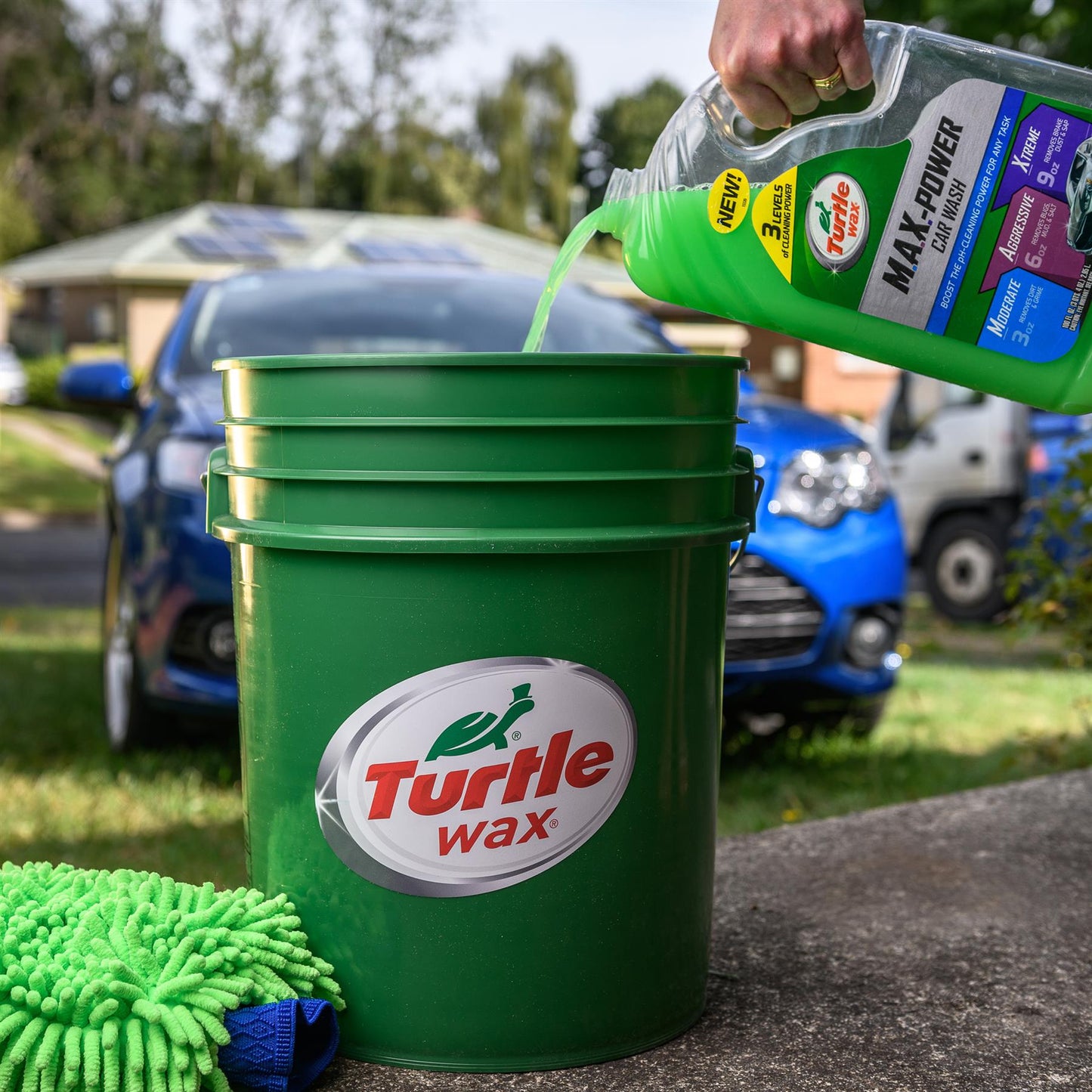Car wash liquid being poured from a Turtle Wax bottle into a bucket with a Turtle Wax logo, for car cleaning in India.