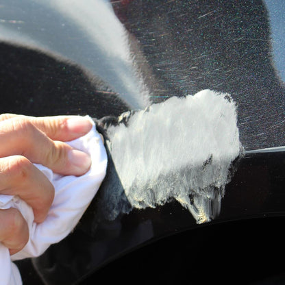 Black car scratch repair in progress. Applying white Turtle Wax scratch remover on car paint with cloth.