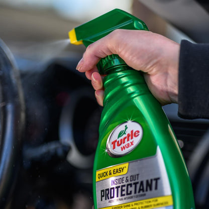 Hand sprays Turtle Wax Inside & Out Protectant on a car interior. The green bottle has a turtle logo.