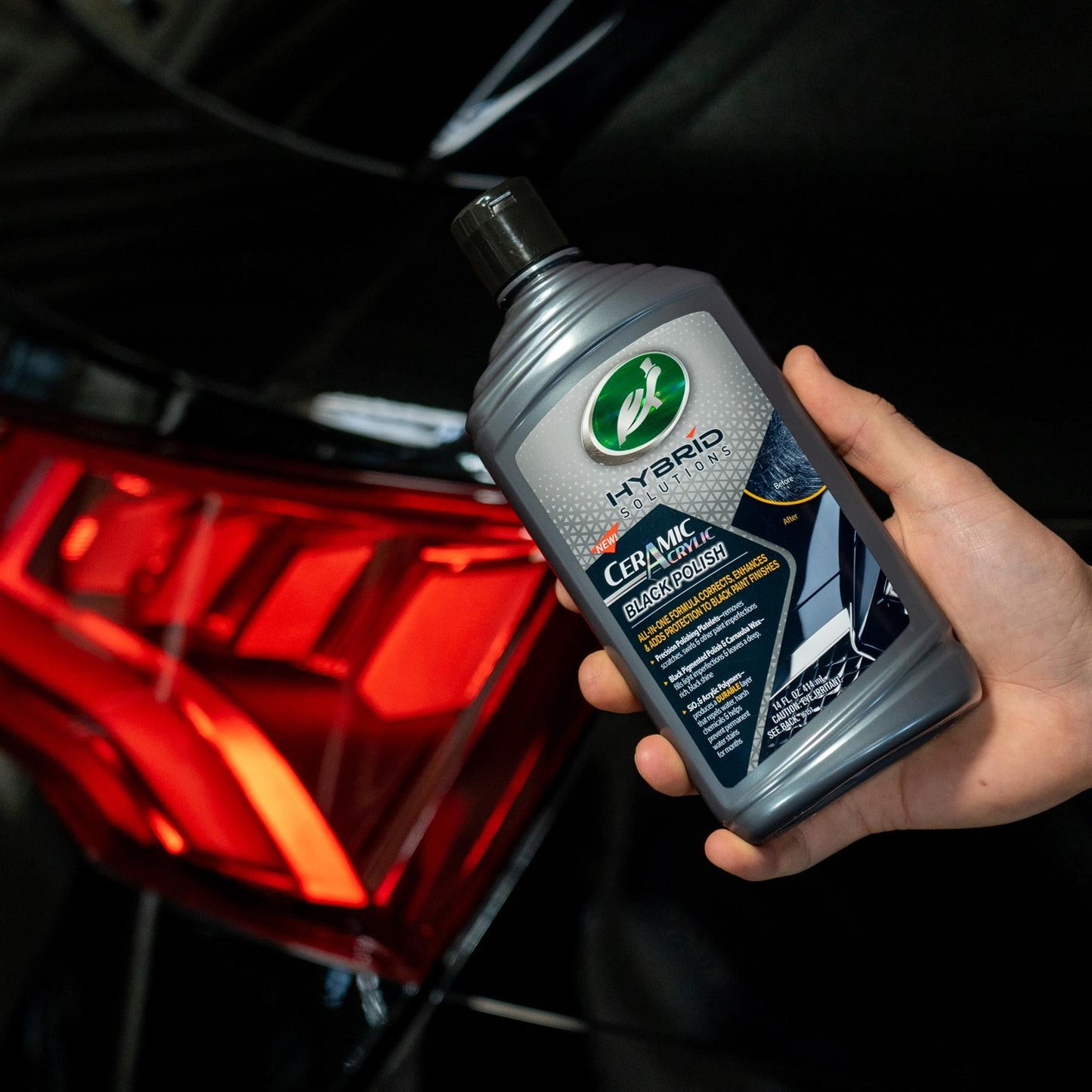 Turtle Wax Hybrid Solutions ceramic acrylic black polish, 414ml, bottle held in hand near a car's tail light. For black car paint.