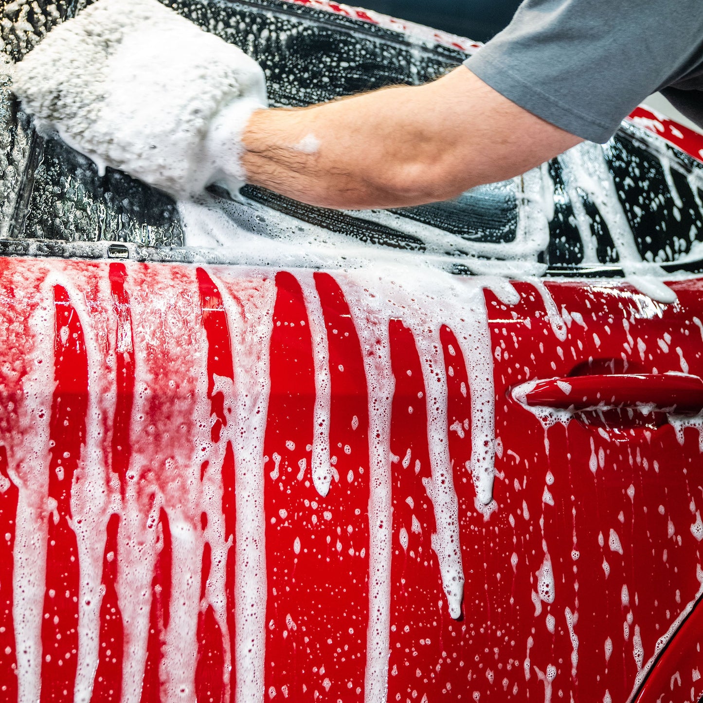 Red car getting washed with foam, using a wash mitt. Man washing car, Turtle Wax product for car care.
