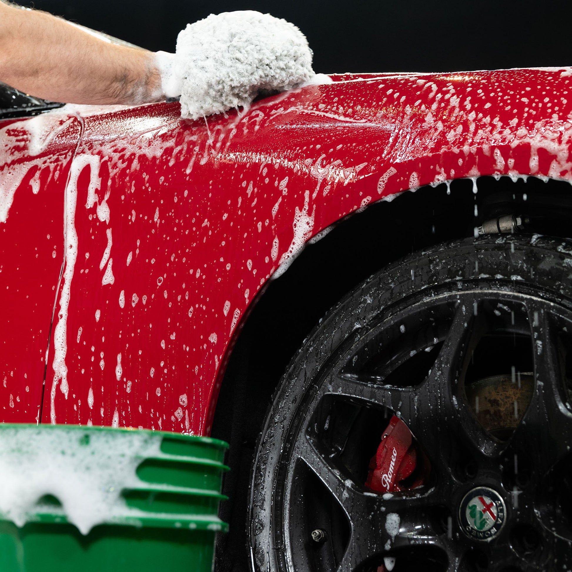 Red car with sudsy foam. Black wheel. Car washing.