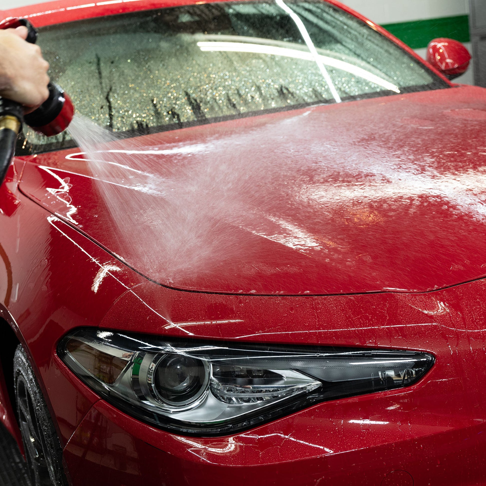 Red car wash: Red car being sprayed with water. Turtle Wax products can help clean and protect your car. #carwash #cardetailing #india
