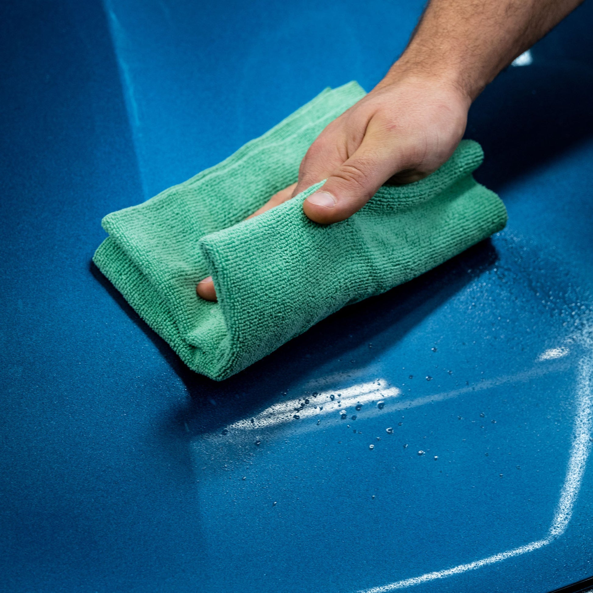Blue car surface being cleaned with a green microfiber cloth. Spotless shine.