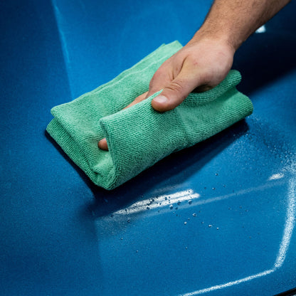 Blue car surface being cleaned with a green microfiber cloth. Spotless shine.
