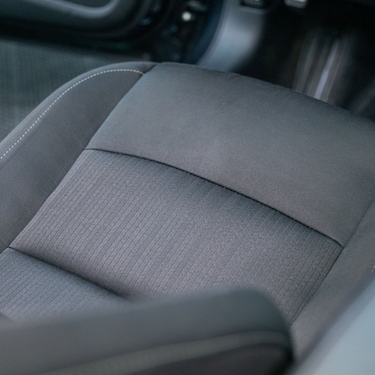 Car seat featuring fabric in a dark tone, showcasing detailing like stitching.
