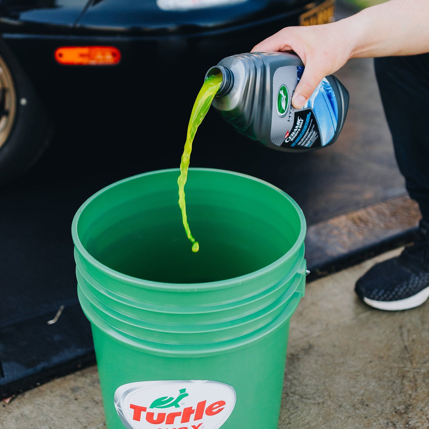 A person pouring Turtle Wax ceramic wash into a bucket; car wash prep shown. #TurtleWax #carcare #India