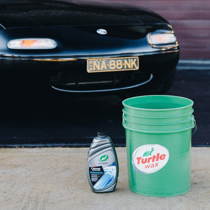 Black car, bucket with Turtle Wax logo, & car wash liquid bottle. Car care items for vehicle cleaning in India.