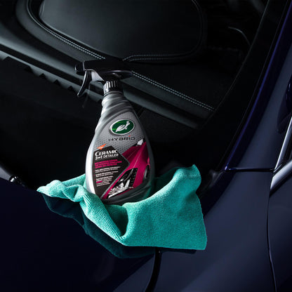 Turtle Wax Hybrid Solutions Ceramic 3-in-1 Detailer (946ml) with microfibre cloth on a shiny blue car's hood, for car detailing.