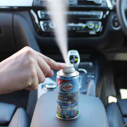 Hand sprays Turtle Wax Odor-X into a car interior. The can is on the console of an Indian vehicle.